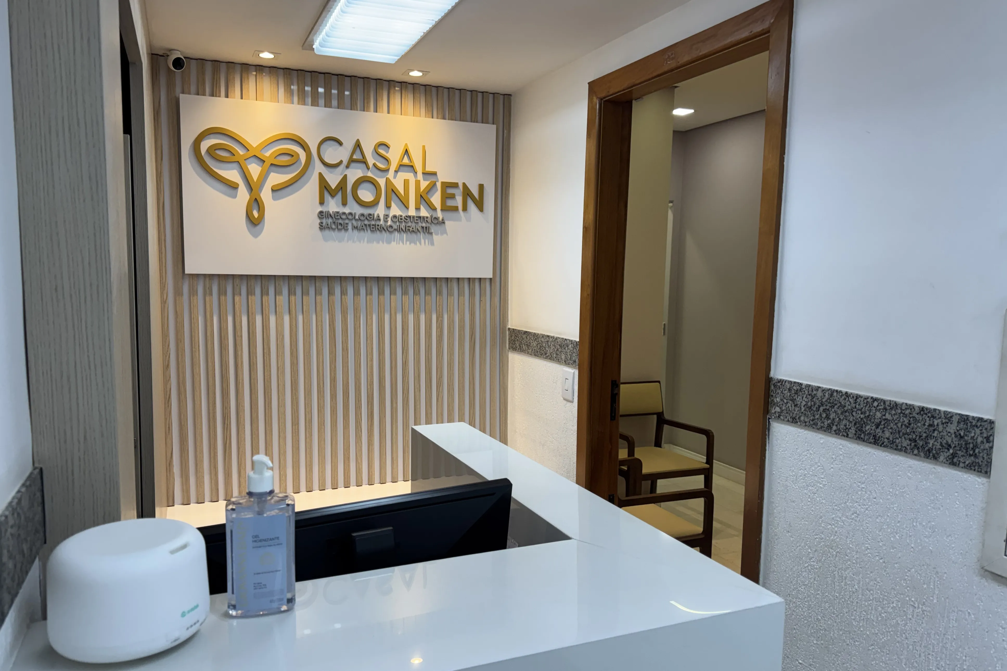 Recepção da clínica: painel ripado com a logo dourada e balcão